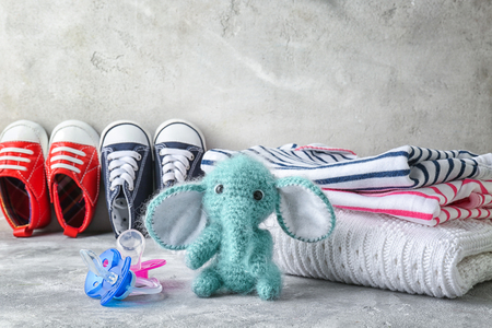 Knitted toy elephant, baby clothes and pacifiers on light gray backgroundの写真素材