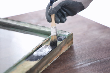 Worker painting frame of old window lying on wooden table, closeupの写真素材