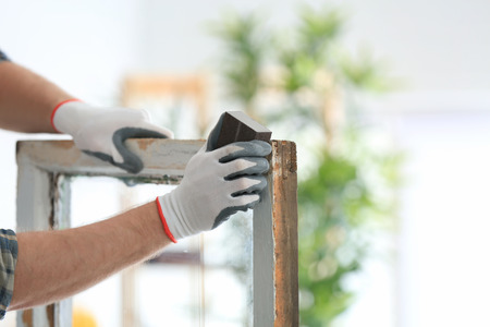 Worker grinding surface of old window frame with abrasive stone, closeup