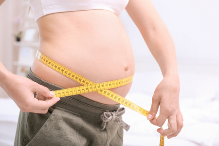 Pregnant woman measuring her belly at home. Pregnancy weight gain conceptの写真素材