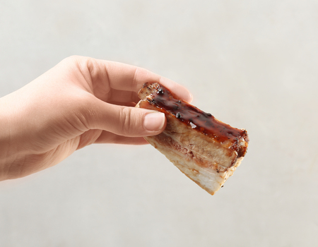 Female hand holding delicious pork ribs on light backgroundの写真素材