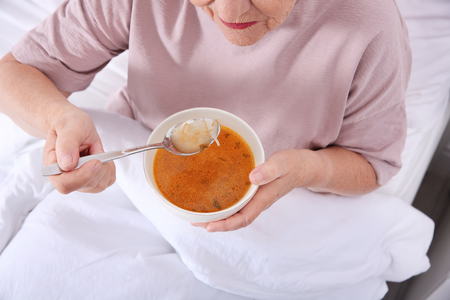 Elderly woman sitting in bed and eating soup, closeupの写真素材