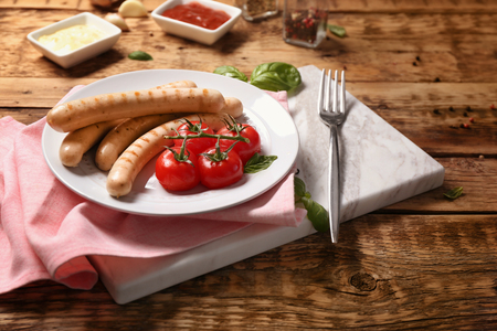 Plate with roasted sausages and tomatoes on wooden backgroundの写真素材