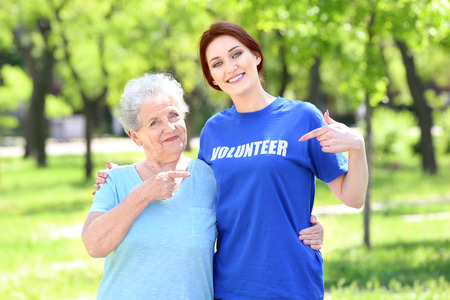 Young and senior woman pointing at t-shirt with text VOLUNTEER outdoorsの写真素材