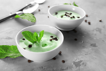 Bowls with delicious mint chocolate chip ice cream and fresh leaves on grey tableの写真素材