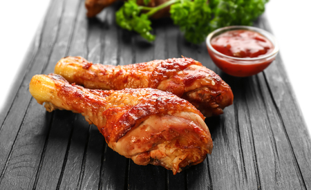 Tasty chicken legs and small bowl with sauce on wooden boardの写真素材