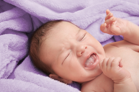 Crying newborn baby boy lying on soft plaid at homeの写真素材
