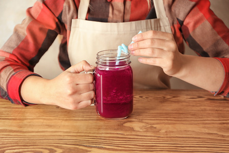Young woman with jar of beet smoothie sitting at wooden tableの写真素材
