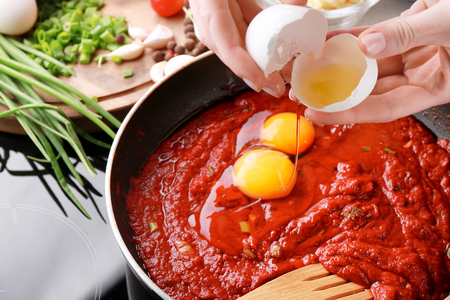 Woman cooking eggs in purgatory on stoveの写真素材