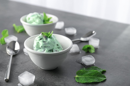 Bowl with delicious mint chocolate chip ice cream and ice cubes on grey tableの写真素材