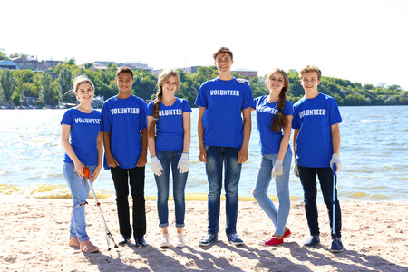 Young people with trash pickers standing on beach near river. Volunteer conceptの写真素材