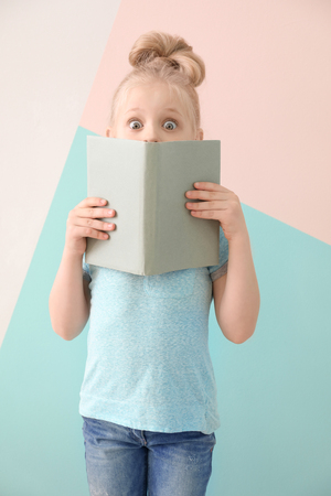 Cute funny girl with book on color backgroundの写真素材