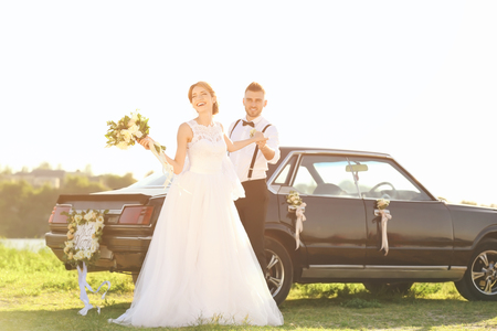 Happy wedding couple near decorated car outdoorsの写真素材
