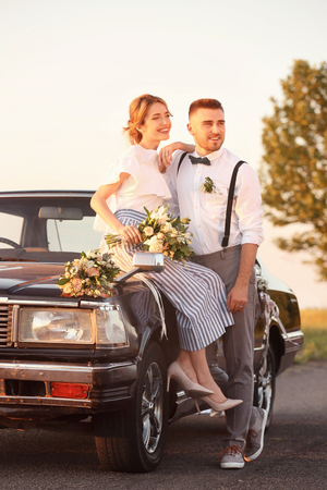 Happy wedding couple and decorated car outdoorsの写真素材