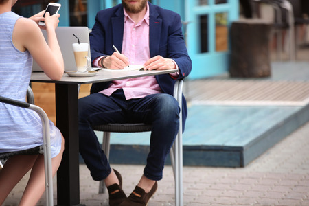 Young blogger with with woman sitting in cafe, outdoorsの写真素材