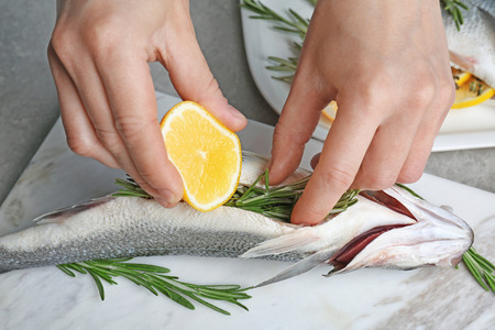 Woman squeezing lemon onto fish stuffed with rosemary on marble board, closeupの写真素材
