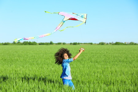 Happy little Afro American girl with kite in green fieldの写真素材