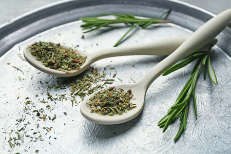 Spoons with dried herbs and fresh rosemary on metal plateの写真素材