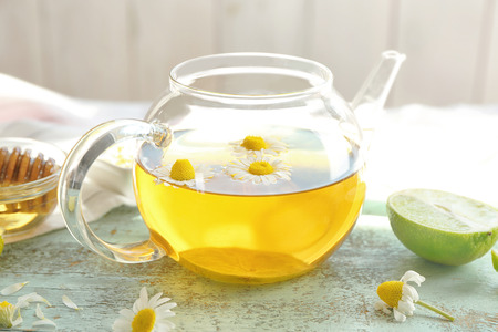 Glass teapot with tasty chamomile tea on color wooden tableの写真素材