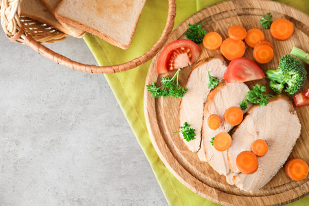 Cutting board with delicious sliced turkey fillet and vegetables on tableの写真素材