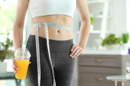 Young woman with measuring tape and juice at home. Diet conceptの写真素材