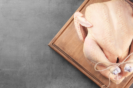 Wooden board with whole raw turkey on grey backgroundの写真素材