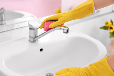 Female hands with sponge cleaning a tap in the bathroomの写真素材