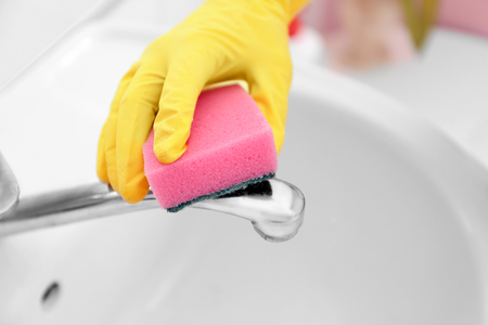 Female hand with sponge cleaning a tap in the bathroomの写真素材