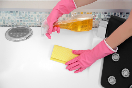 Female hands with sponge cloth and detergent spray cleaning a bath in the bathroomの写真素材