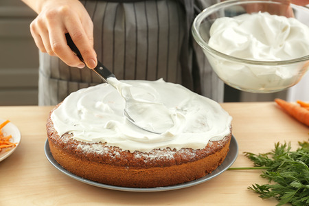 Woman smearing cream on carrot cake in kitchenの写真素材