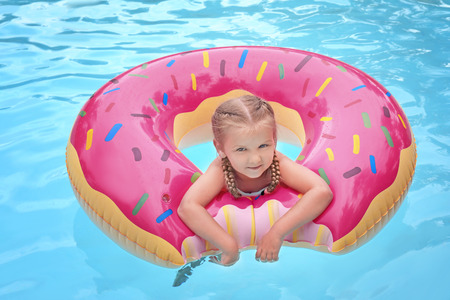 Cute little girl with inflatable donut in swimming pool