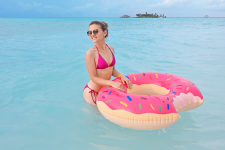 Beautiful young woman bathing with colorful inflatable donut at resort