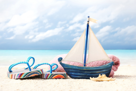 Toy ship, flip-flops and towel on sand near sea. Summer vacation conceptの写真素材