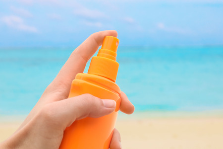 Female hand with bottle of sunscreen cream and blurred sea beach on background. Summer vacation conceptの写真素材