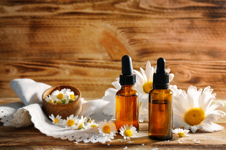 Bottles of essential oil and chamomile flowers on wooden tableの写真素材