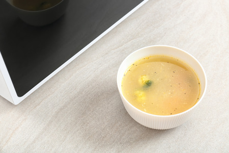 Bowl with soup near microwave on tableの写真素材