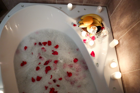 Bathtub filled with foam and rose petals prepared for romantic dateの写真素材