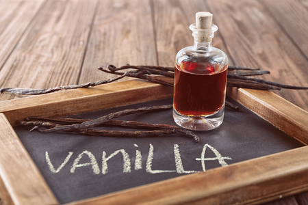 Dry vanilla beans and bottle with aromatic extract on boardの写真素材