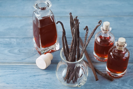 Bottles with aromatic extract and dry vanilla beans in jug on tableの写真素材