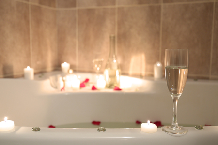Glass with alcoholic drink and candles for romantic date on tub lipの写真素材