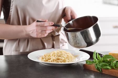 Woman adding tasty tomato sauce to pasta on plateの写真素材