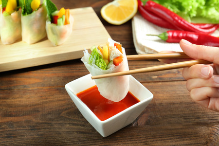 Female hand holding delicious spring roll with chopsticks