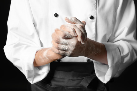Young female chef with hands in flour on dark background, closeupの写真素材