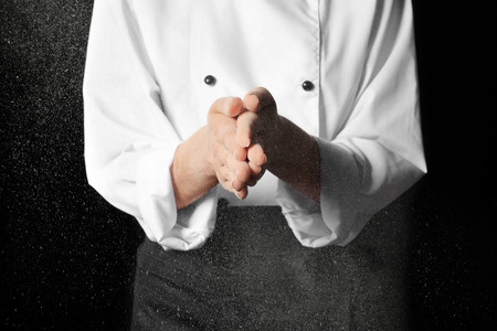 Young female chef with hands in flour on dark background, closeupの写真素材