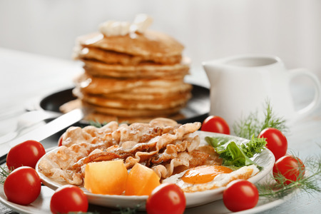 Tasty breakfast with fried egg, bacon and pancakes on tableの写真素材