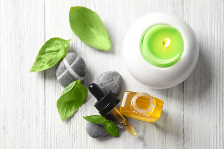 Bottle with basil oil, green leaves and candle on wooden tableの写真素材