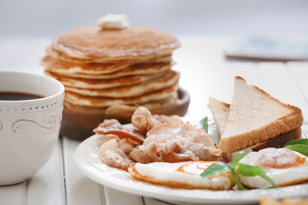 Tasty breakfast with fried eggs, pancakes, bacon and cup of coffee on tableの写真素材
