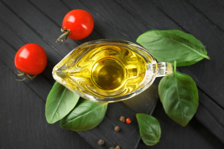 Gravy boat with basil oil, green leaves and tomatoes on wooden boardの写真素材
