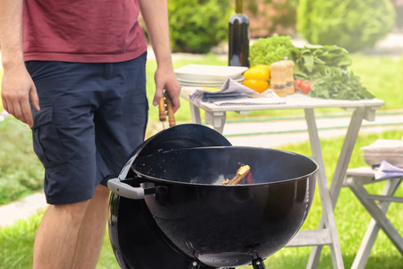 Young man standing near barbecue grill outdoorsの写真素材