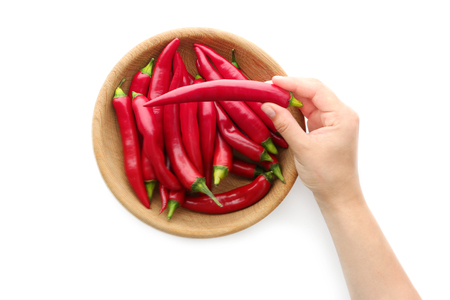 Woman's hand taking red chili pepper out of bowl isolated on whiteの写真素材